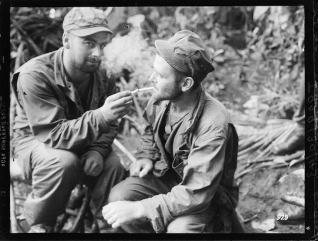 Two WWII soldiers smoking cigarettes in the forest.