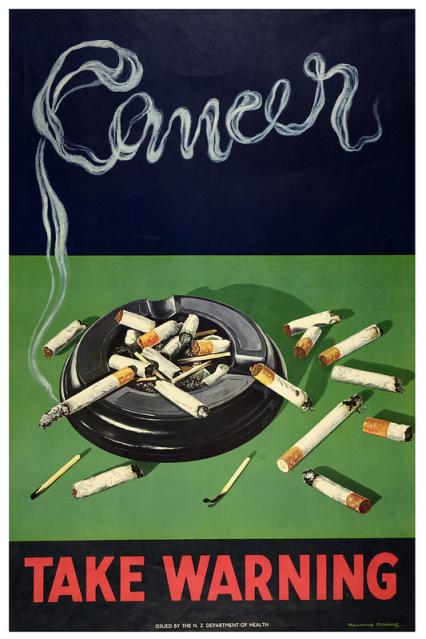 A poster shows an illustrated ash tray with cigarettes inside it. The word "cancer" is written in stylised cigarette smoke. The phrase "take warning" appears in bold red text.