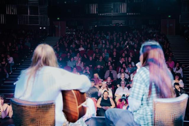 The backs of musicians chontalle musson, Smokefree rockquest 2024 finalists performing on a stage, facing an audience