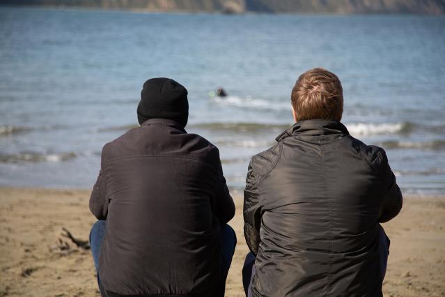 Two figures side by side facing a beach