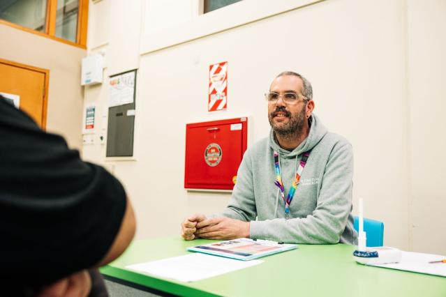 A person at a desk with a lanyard, looking up at someone they are supporting