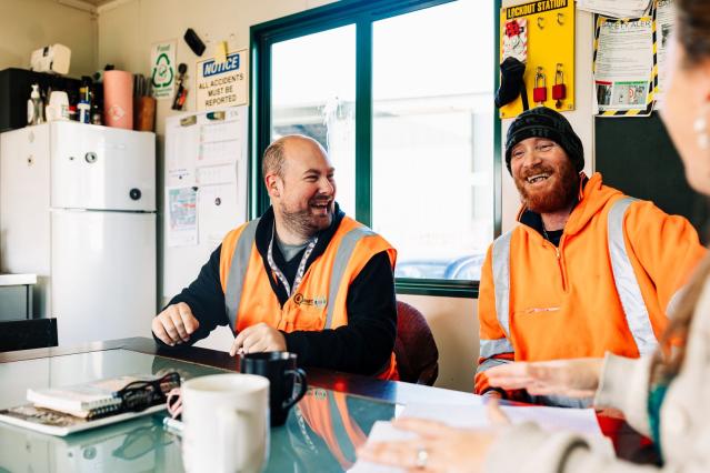 Two men in high vis gear at a desk, laughing together