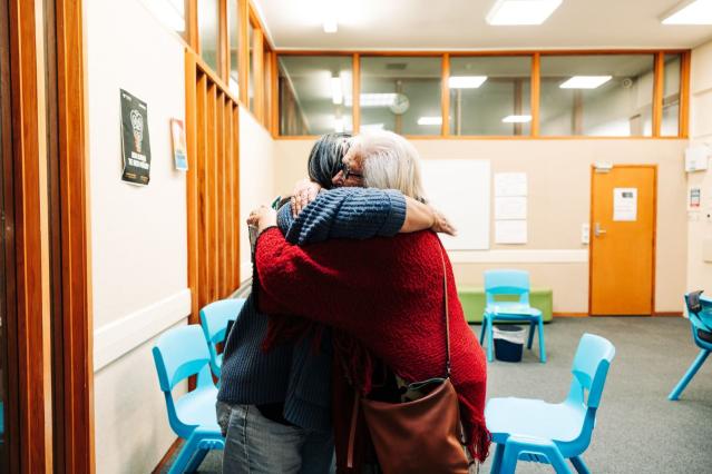 Two people embracing in a room with desks and chairs