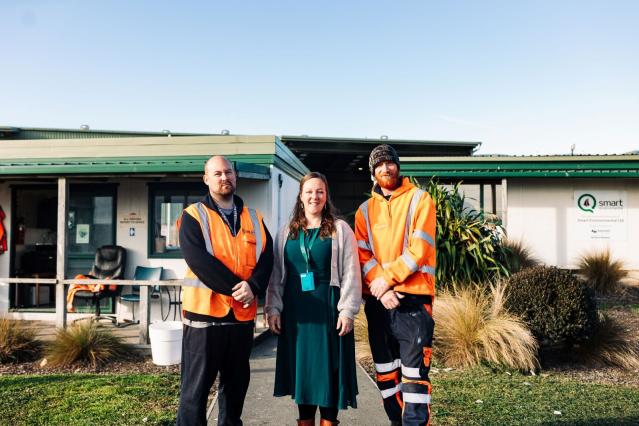 A woman wearing a lanyard stands between two men in high vis gear